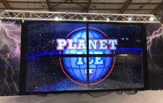 One side of the 'Dizzytron' showing four screens. Screens showing the Planet Ice Logo.